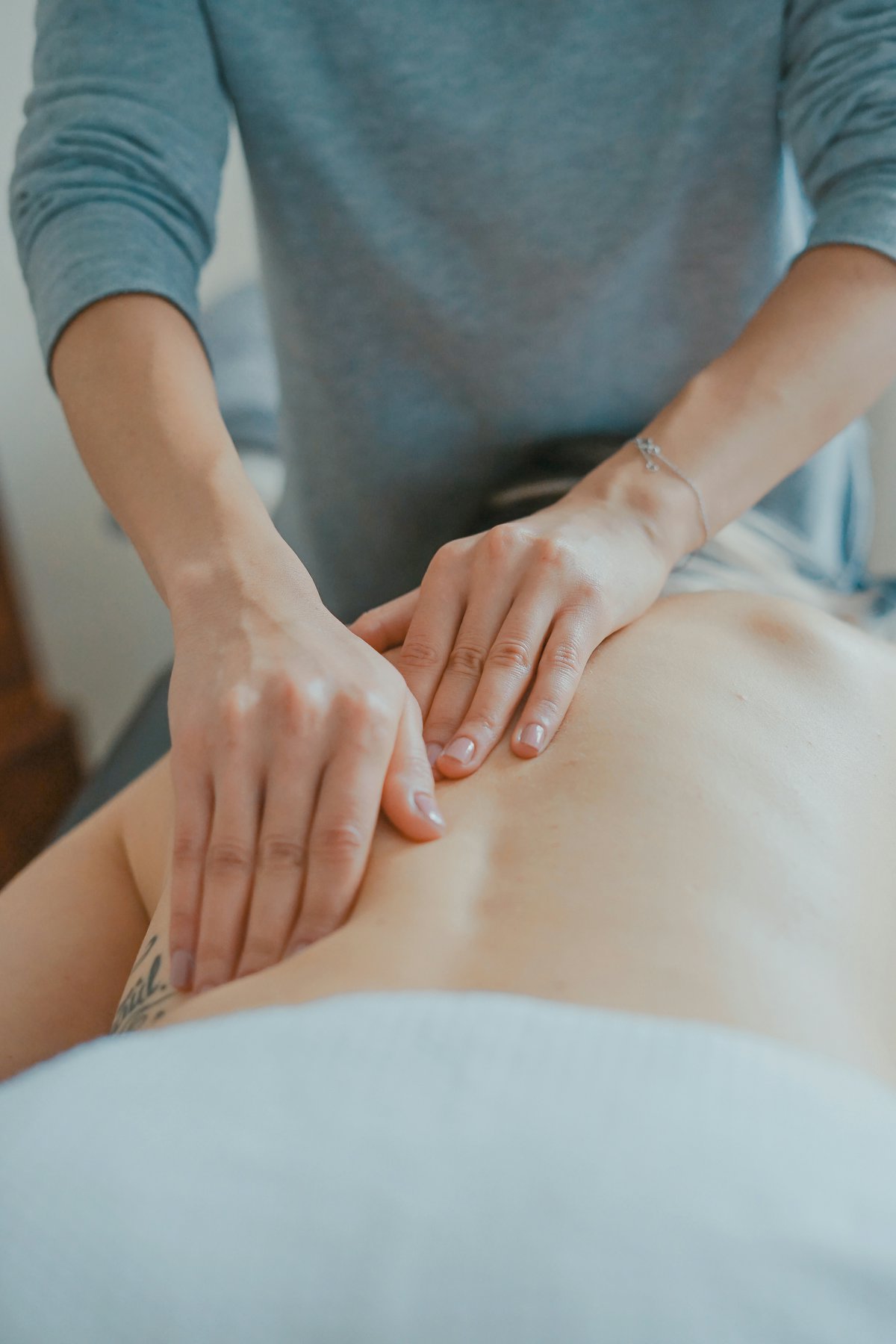Therapeutin behandelt mit beiden Händen den unteren Rücken einer liegenden Patientin
